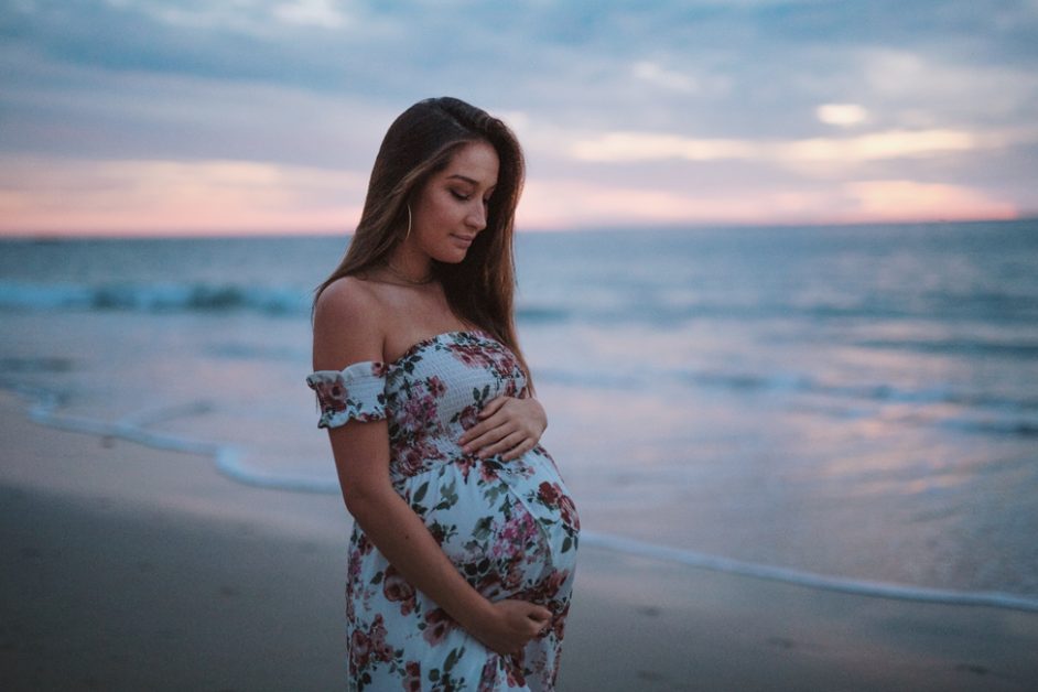 a woman holding her pregnant belly at the beach
