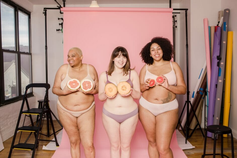 3 women in their undergarments holding up a fruit posing in a photo studio room