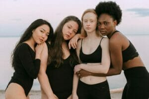 4 women in black shape wears posing with the beach as backdrop