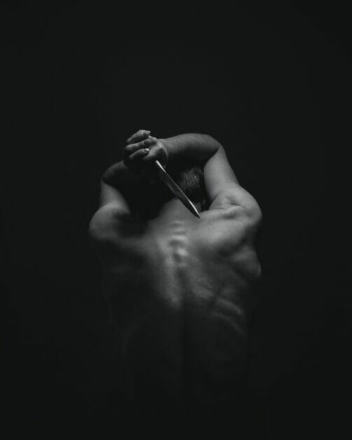 a man holding a knife aimed at his naked back