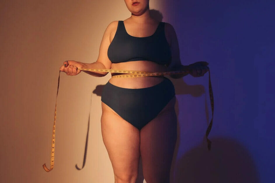 a plus-size woman in shaperwear holding a tape measure along her waistline