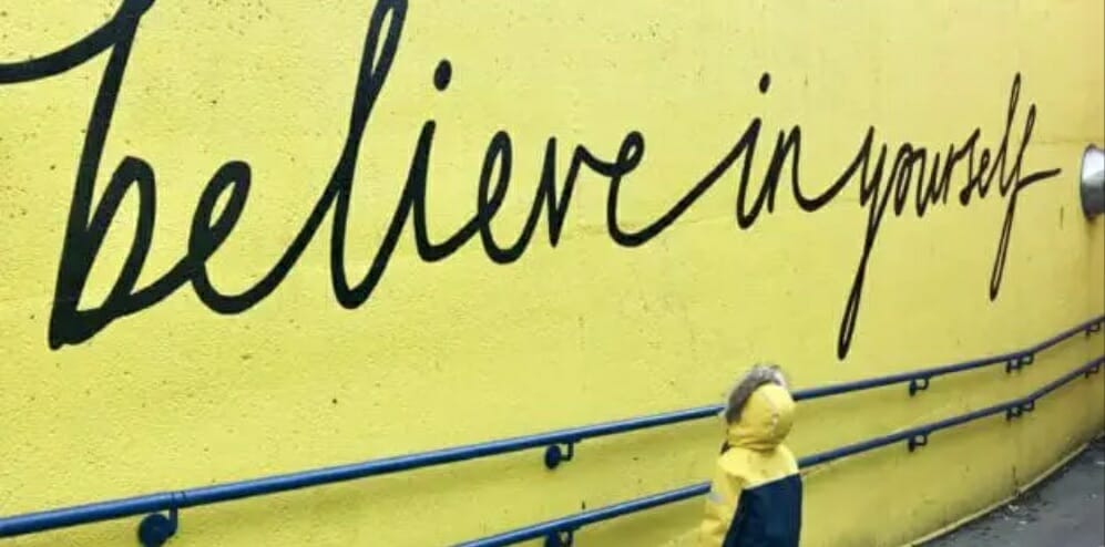 believe in yourself printed on a yellow wall with a child looking up