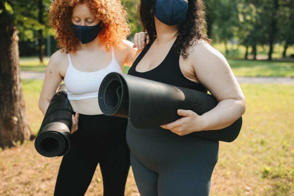 two woman in facemask holding a yoga mat