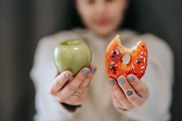 woman holding an apple and a doughnut