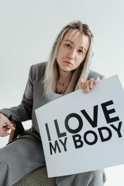 woman seating and holding a placard with a message: I LOVE MY BODY