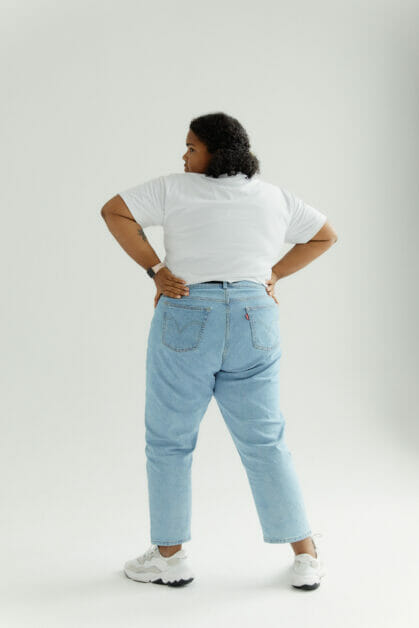 a plus-size woman wearing high-rise waisted jeans and white tee posing on her back