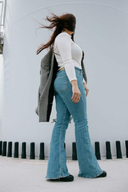 a woman wearing white long sleeve with coat on her shoulder paired with bootcut or flared leg jeans and a black shoes