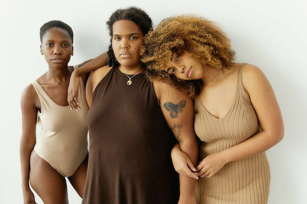 three women wearing a brown shade one piece, dress, and bodycon