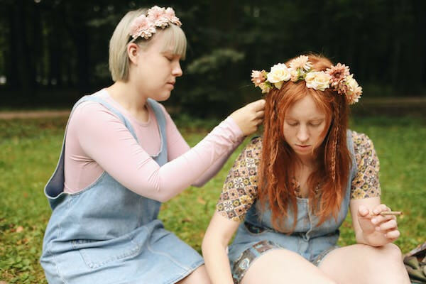 two women sitting on the grass with a flower headress