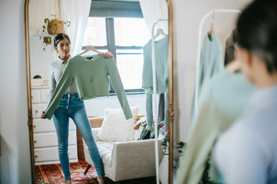 woman in a fitted jeans and long sleeve top checking out another long sleeve top in the mirror of a boutique shop