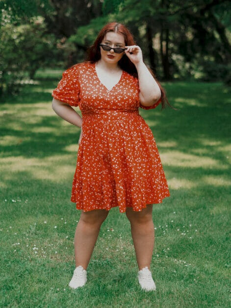 woman in plus-size wearing an overflowing red dress posing at the green outdoors