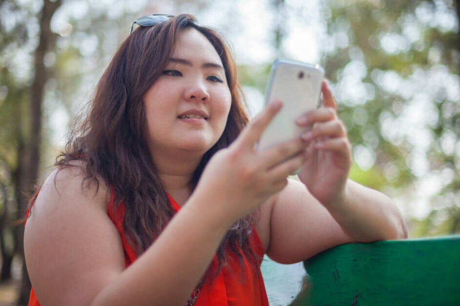 a plus size woman sitting on the outdoor and using her white smartphone