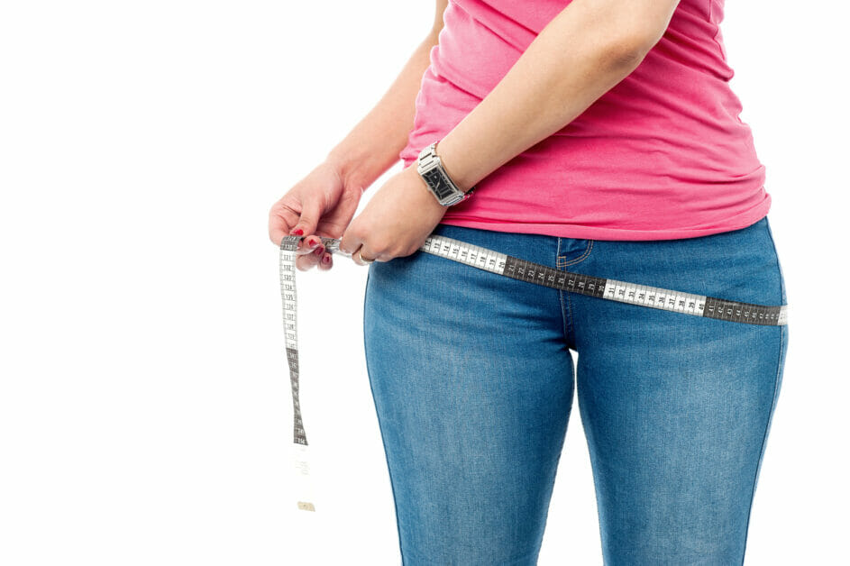 woman in a pink shirt and blue denim measuring her hips area with a measuring tape