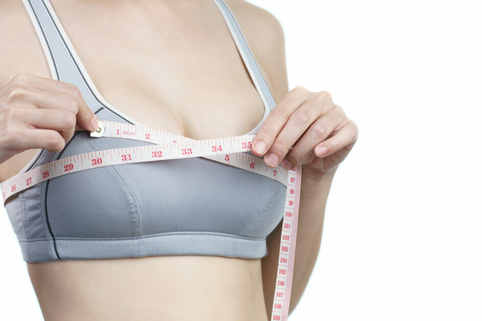 woman in a sports bra measuring her bust area with a measuring tape