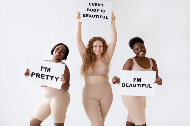 three women holding placards with body positivity statements